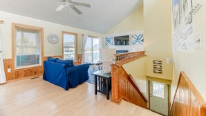 A spacious living room with a wooden floor, a ceiling fan, and a staircase with a wooden railing. - Pet-friendly oceanside Corolla home w/ private pool & hot tub! (Corolla)