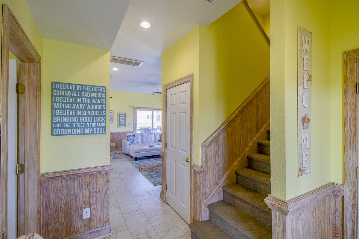 A hallway with a wooden staircase, a welcome sign, and a wall with a motivational quote.