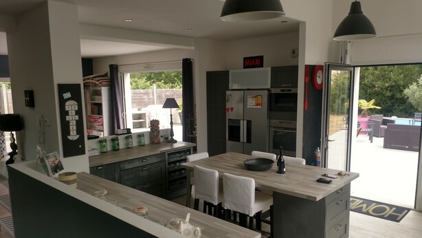 A modern kitchen with a central island, built-in appliances, and a dining area with white chairs.