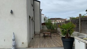 A rooftop patio with a wooden deck, a potted plant, a metal table, and a white cabinet.