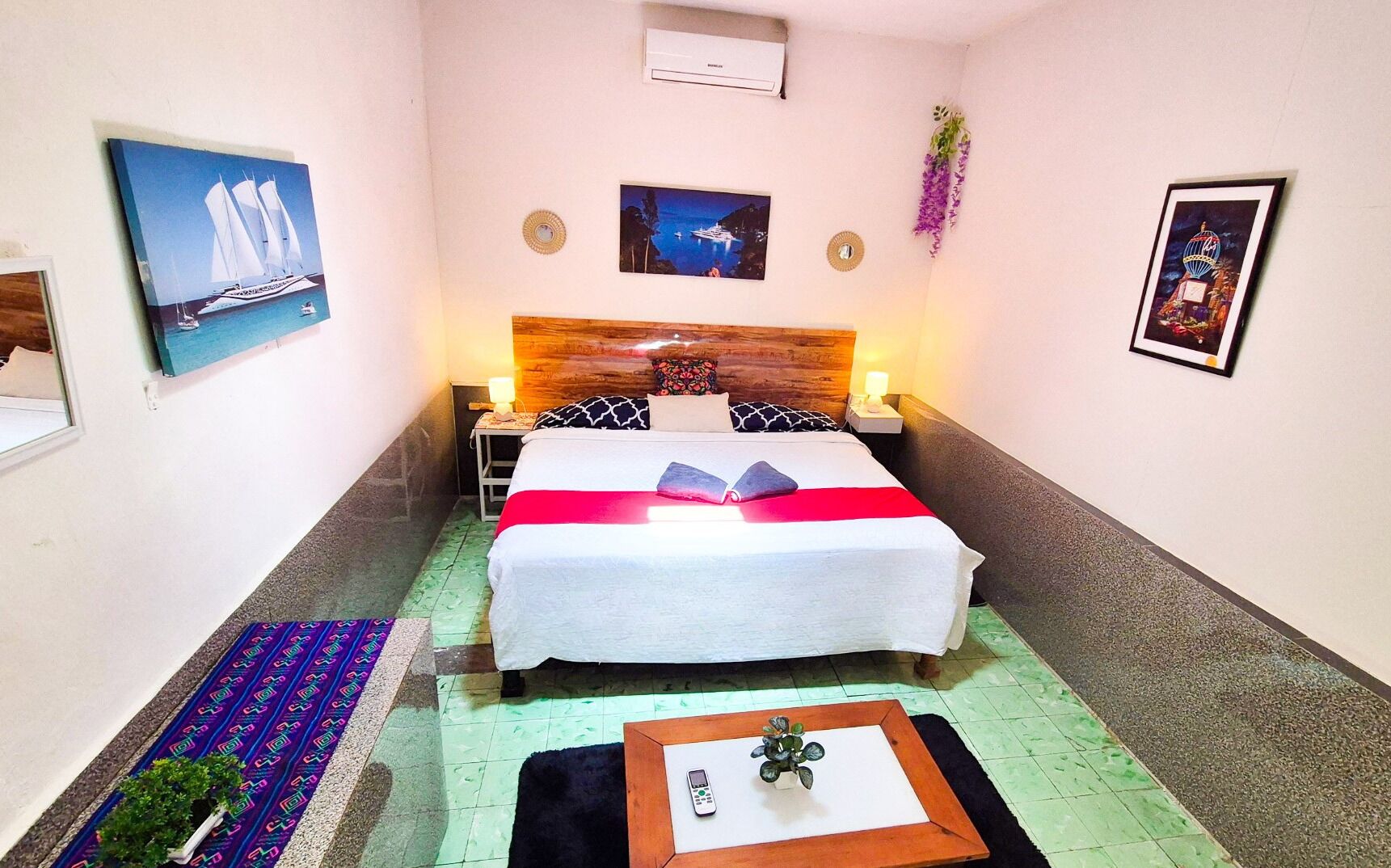 Une chambre d’hôtel comprenant un lit, des tables de chevet, une petite table d’appoint, une petite table avec une plante et un climatiseur fixé au mur.