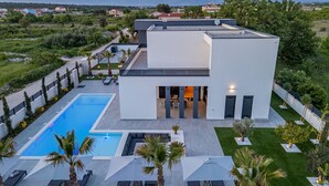 Une maison moderne à deux étages, dotée d’une piscine, d’un espace salon extérieur et offrant une vue sur les montagnes.