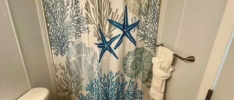 A bathroom with a shower curtain featuring a coral reef design, a toilet, and a towel rack.