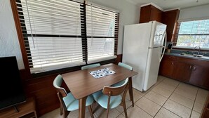 A compact kitchen with a dining table, chairs, a refrigerator, and a window with blinds. - One Particular Cottage - Next to Margaritaville (Fort Myers Beach)