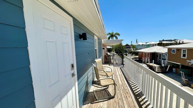 A wooden deck with chairs, a white door, and a view of neighboring houses. - One Particular Cottage - Next to Margaritaville (Fort Myers Beach)