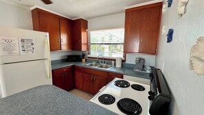 A compact kitchen with wooden cabinets, a white refrigerator, a stove, and a sink. - One Particular Cottage - Next to Margaritaville (Fort Myers Beach)