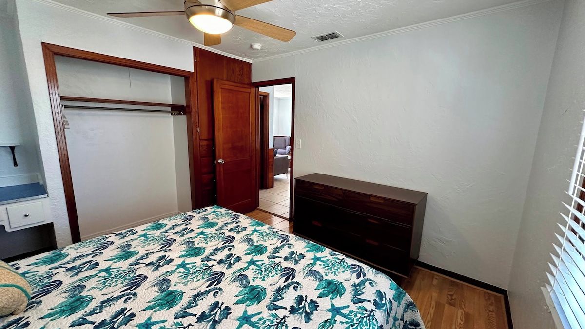 A bedroom with a bed, a dresser, a closet, and a ceiling fan.