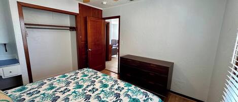 A bedroom with a bed, a dresser, a closet, and a ceiling fan.
