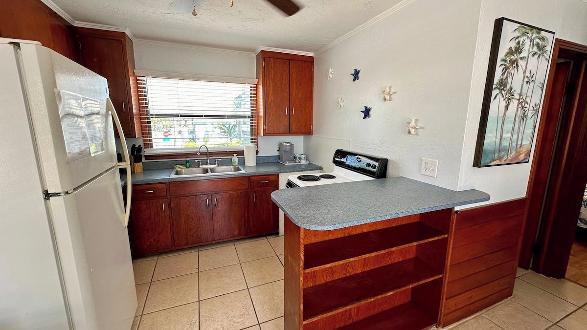 Une cuisine de taille réduite, avec des meubles de rangement en bois, un réfrigérateur blanc, une cuisinière et un évier.