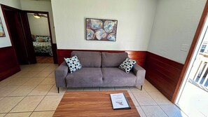 A room with a grey sofa, two patterned pillows, a wooden coffee table with a book, and a painting on the wall.