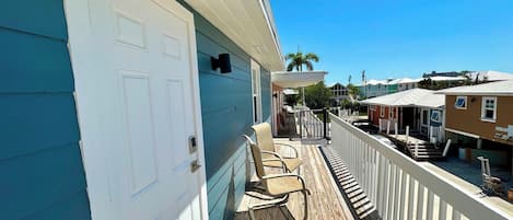 Una terraza de madera con asientos exteriores, una puerta blanca y vistas a casas vecinas.