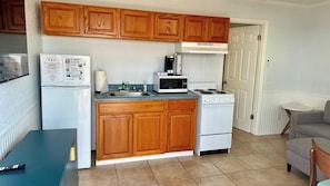 A compact kitchen with wooden cabinets, a refrigerator, a microwave, a stove, and a sink.