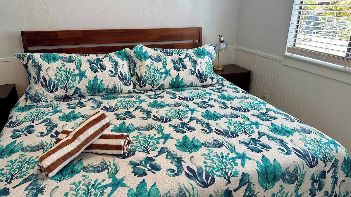 A bed with a floral bedspread, two pillows, and two striped towels.