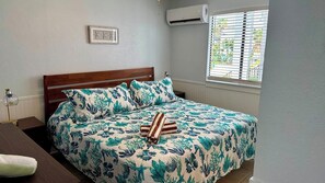 Un lit avec une couvre-lit à motifs floraux, une tête de lit en bois et une fenêtre avec des stores.