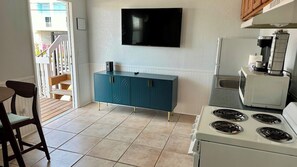 A compact kitchen with a white stove, teal cabinetry, and a flat-screen TV mounted above the counter.