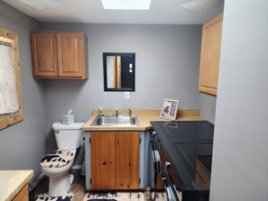 Une cuisine compacte comprenant un évier, des placards en bois, des toilettes et une cuisinière noire.