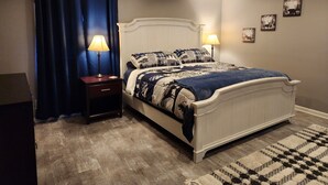 A bedroom with a bed, two bedside tables, a nightstand, a blue curtain, and a patterned rug. - Cabin in Oscoda with hot tub and game room

 (Oscoda)