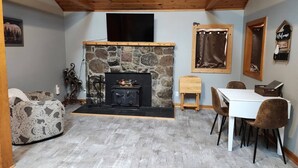 A cozy room with a stone fireplace, a dining table with chairs, and a wooden ceiling. - Cabin in Oscoda with hot tub and game room

 (Oscoda)