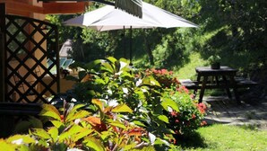 Un espace jardin aménagé avec une table et des chaises en bois, une clôture en treillis et un parasol blanc offrant de l’ombre.