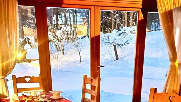 Un coin repas accueillant, avec une table dressée pour deux personnes, agrémentée d’une nappe rouge, d’assiettes, de tasses et d’un panier de pain.