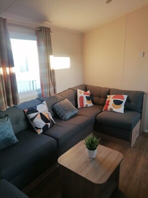 A modern living room with a sectional sofa, multiple cushions, a small wooden coffee table, and a potted plant. - 4-bedroom Caravan/static Home in Clacton-on-sea (Clacton-on-Sea)