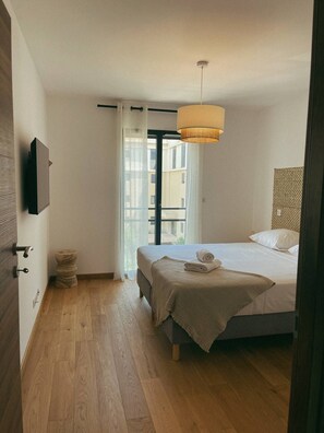 Un dormitorio con una cama, suelo de madera, una ventana con cortinas y una lámpara colgante.