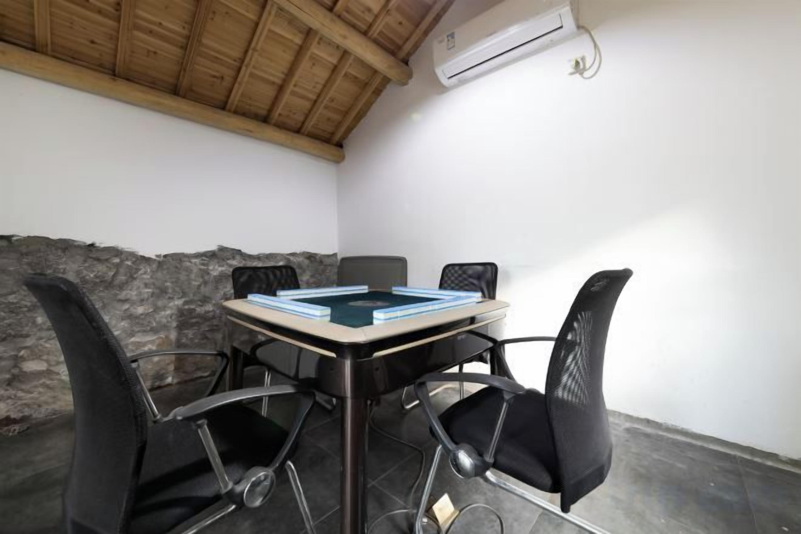 Una habitación con una mesa, sillas, pared de piedra y techo de madera.