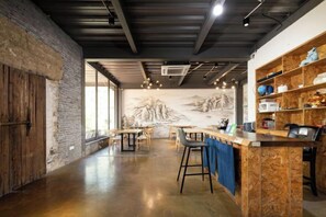 Un interior espacioso con una zona de bar, estanterías de madera y un mural en la pared.