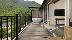 Un balcón con terraza de madera, una bañera blanca, sillas de mimbre y un televisor.