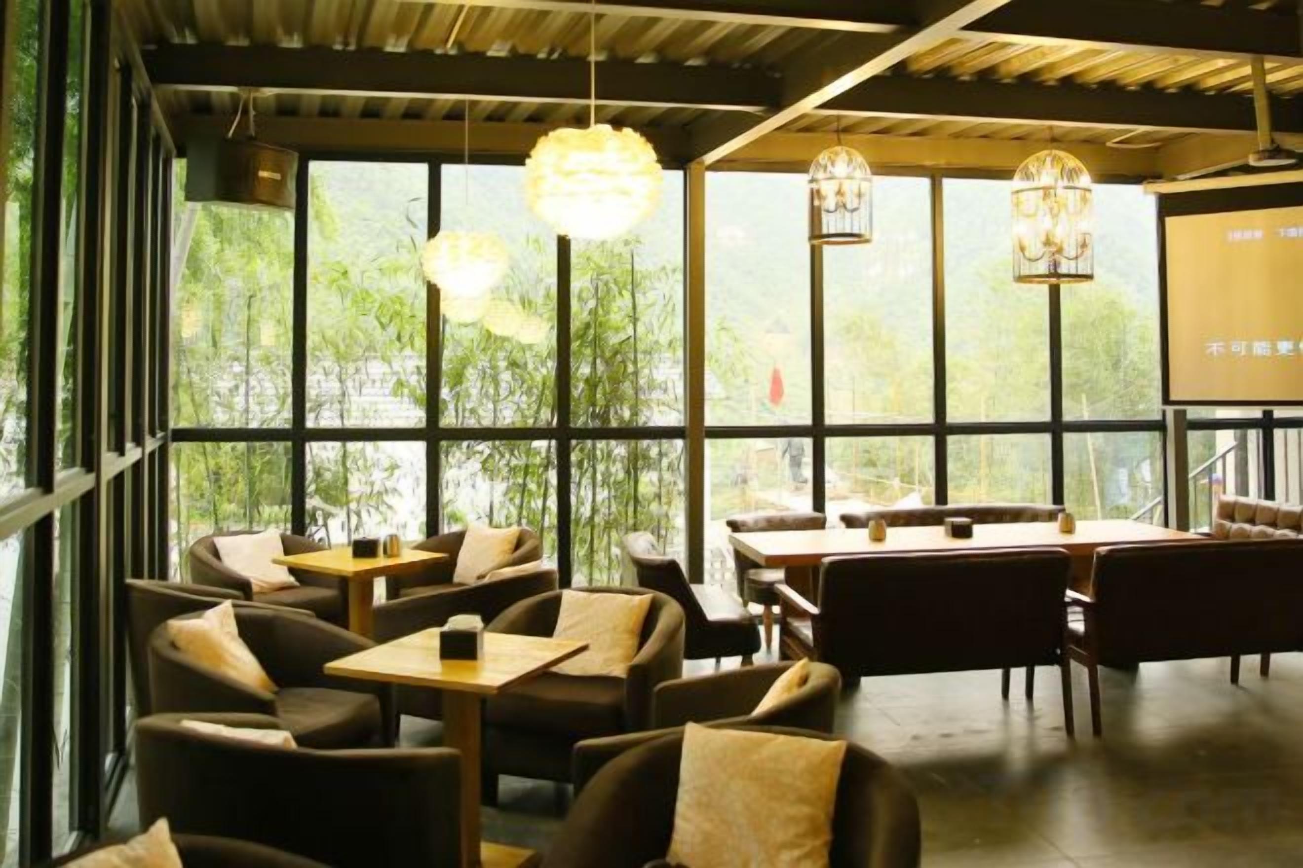 Un restaurant avec des tables et des chaises disposées pour accueillir les clients, de grandes fenêtres laissant entrer la lumière naturelle et des lampes suspendues.