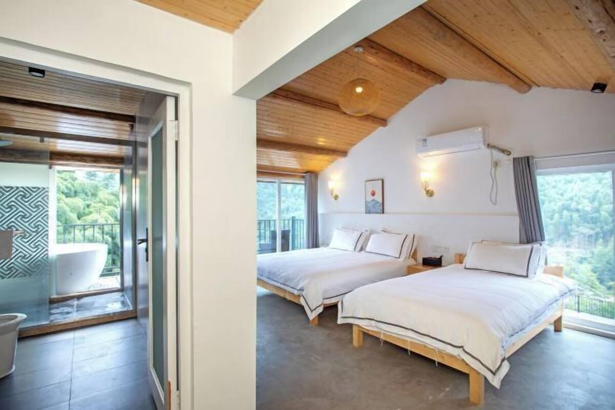Een moderne hotelkamer met balkon, twee bedden, een badkuip en een groot raam.