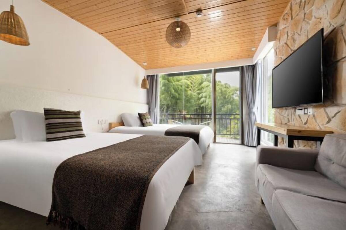 Een moderne hotelkamer met twee bedden, een bank, een televisie en een balkon met uitzicht.