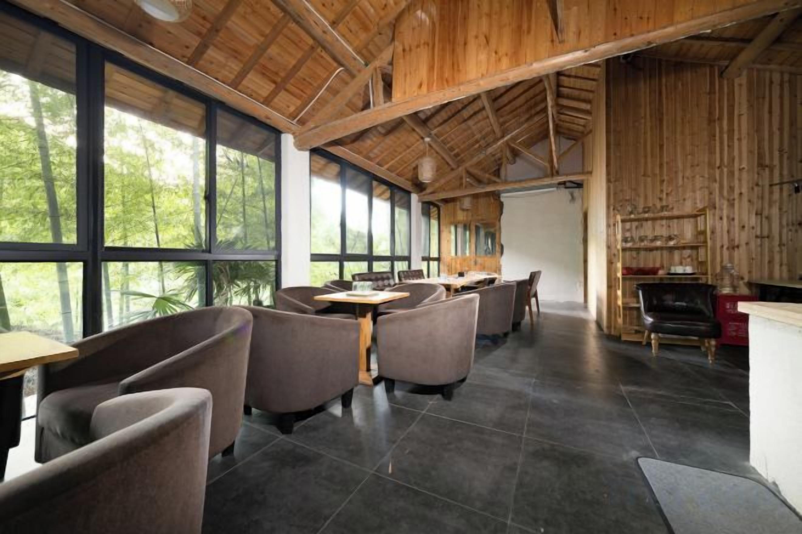 A restaurant with a high ceiling and large windows, providing a view of the outdoors. Tables and chairs are arranged for dining.