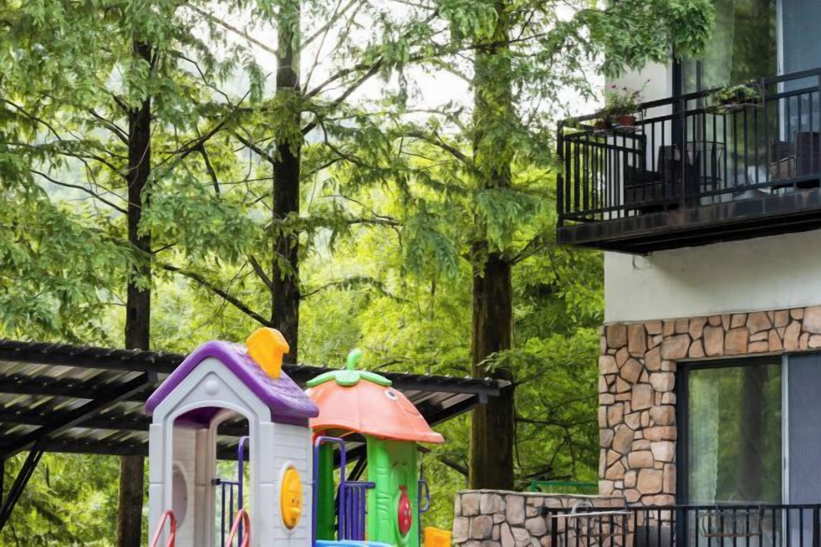 A play structure in a wooded area with a building in the background.