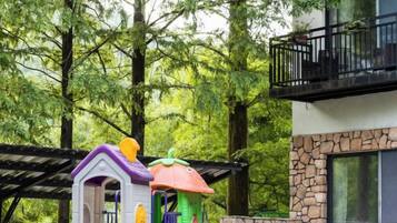 A play structure in a wooded area with a building in the background.
