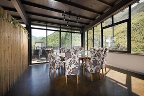 Un comedor con una mesa redonda y sillas, ventanas amplias con vistas a montañas y una pared de madera.