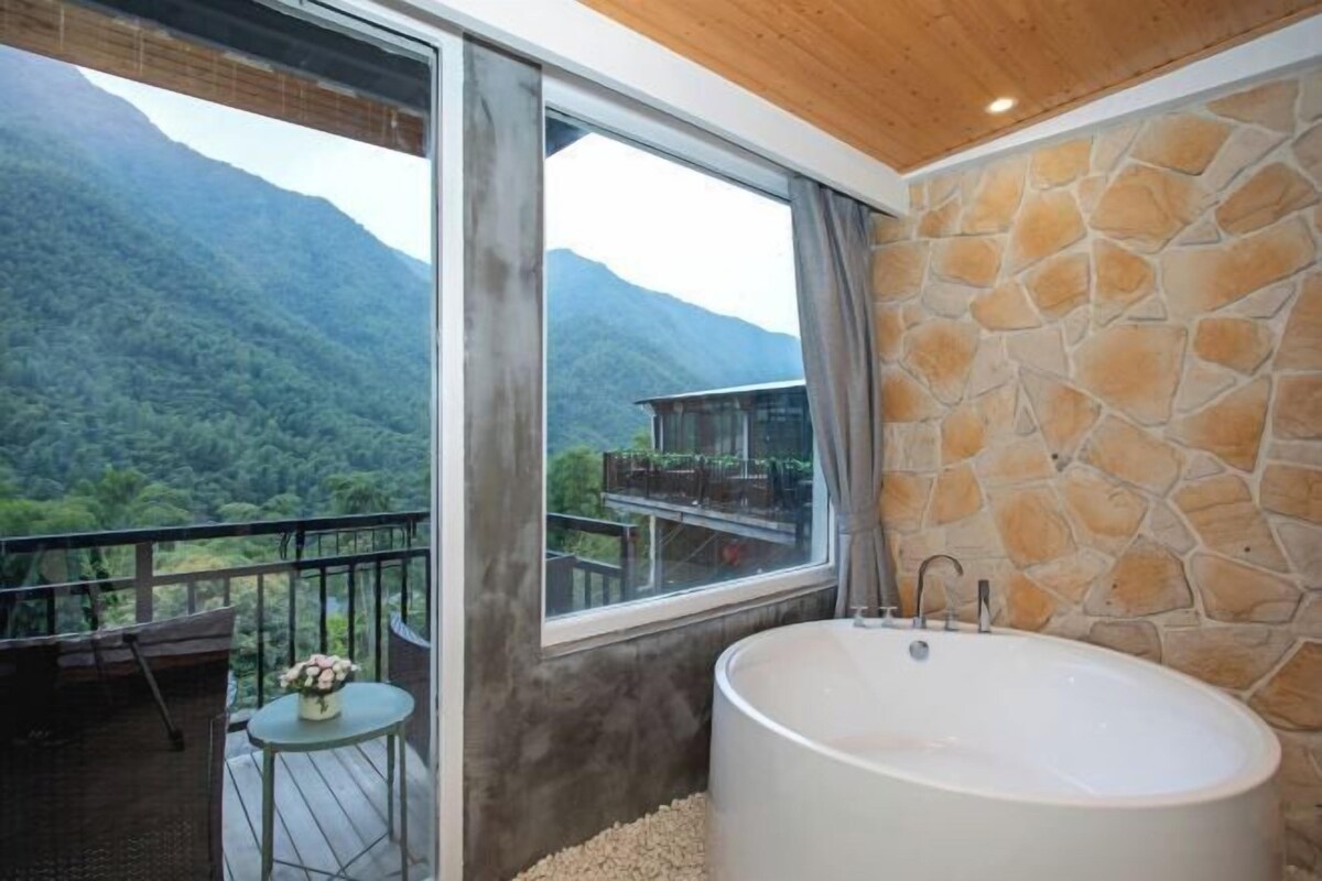 Une salle de bain avec une grande baignoire, une fenêtre donnant sur les montagnes et un mur en pierre.
