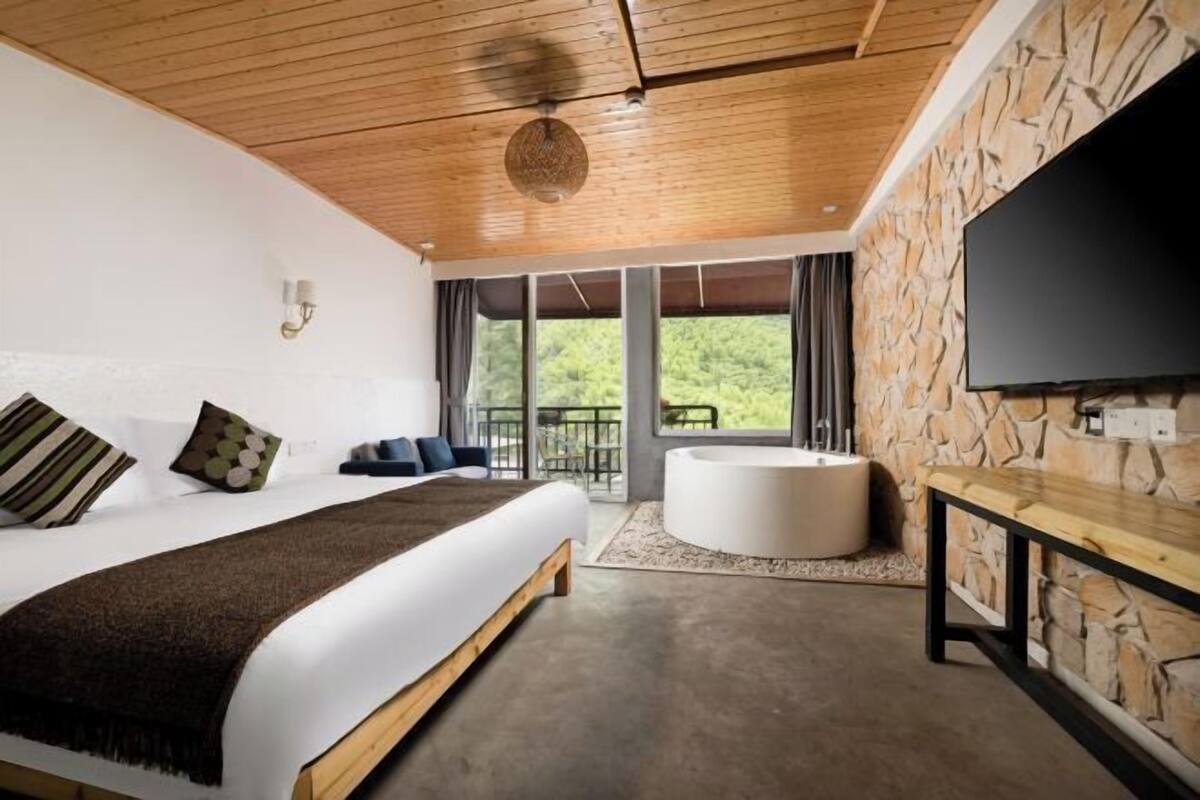 Een slaapkamer met een groot bed, een stenen muur, een flatscreen televisie, een badkuip en een balkon met uitzicht.