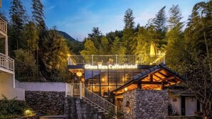 Una moderna estructura de vidrio con el rótulo "Glass Box Coffee Hotel", fachada de piedra, terraza de madera y una escalera que conduce a la entrada.