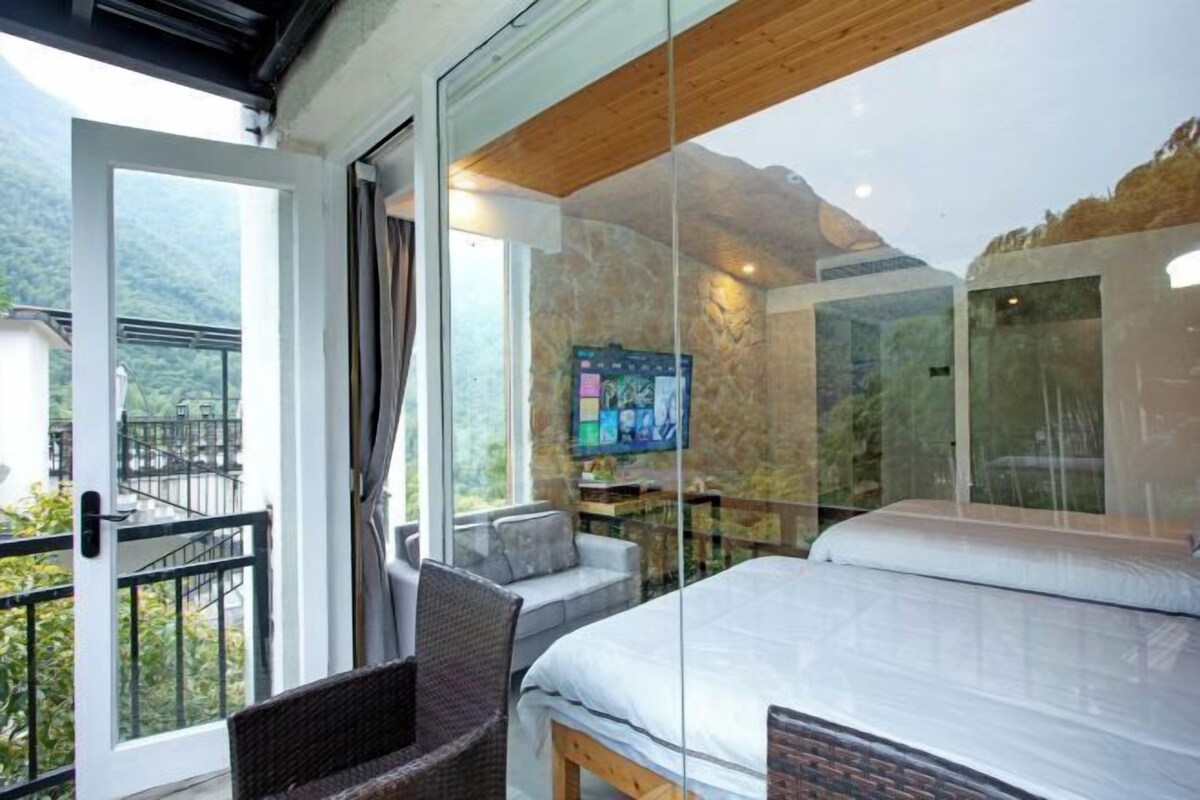 Une chambre à coucher comprenant un lit, un téléviseur et un mur en verre donnant sur une région montagneuse.