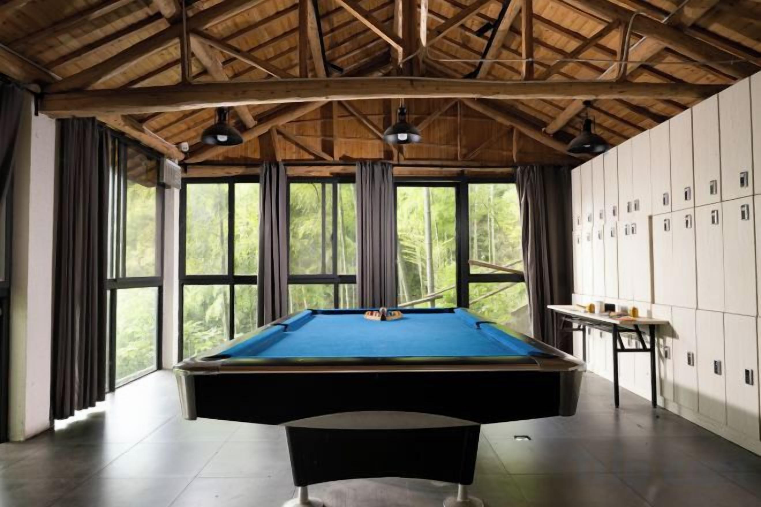 A pool table in a room with a high ceiling and large windows.