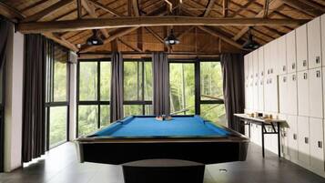 A pool table in a room with a high ceiling and large windows.