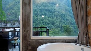 Un baño con una bañera, un ventanal con vistas a zona boscosa y una cortina.