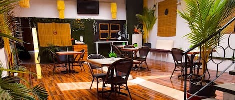 A spacious indoor area with wooden flooring, multiple tables and chairs, and potted plants.