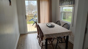 Un comedor con una mesa dispuesta para cuatro, una puerta corrediza de vidrio que da a una terraza y una ventana con un adorno a cuadros.