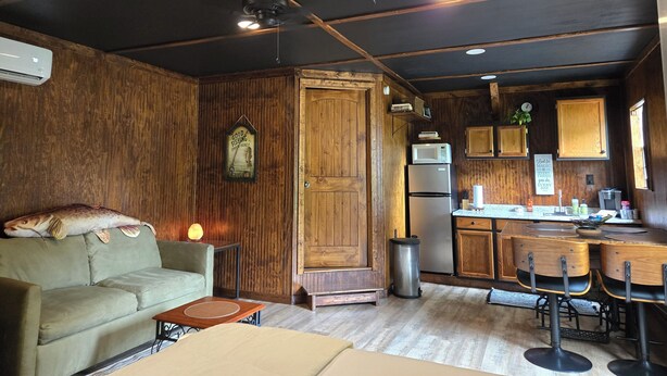 Una habitación acogedora con techo de madera, un sofá, una mesa de comedor con sillas, un refrigerador y un cubo de basura.