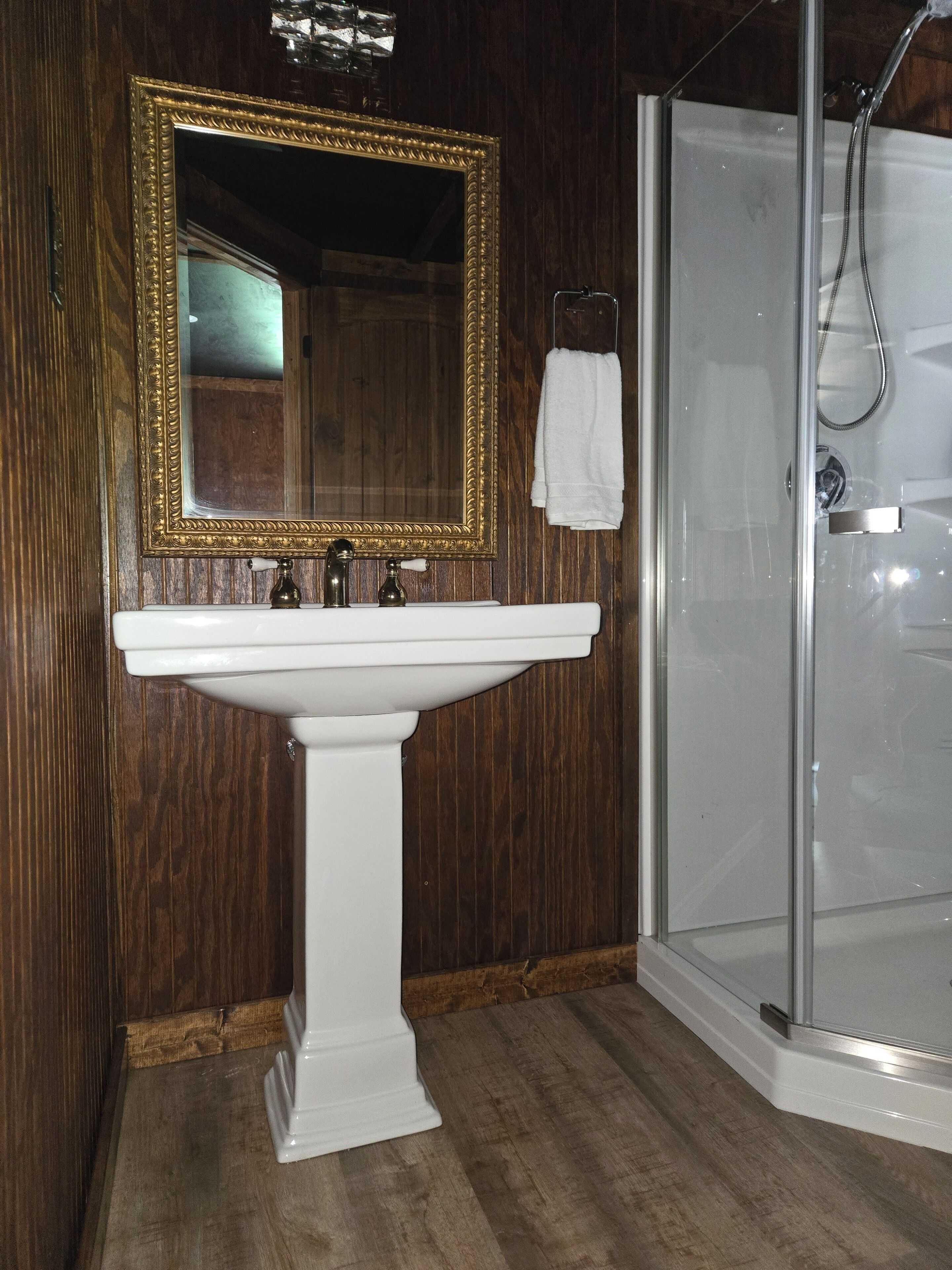 Une salle de bain avec un lavabo sur pied blanc, un miroir à cadre doré et une douche à parois de verre.