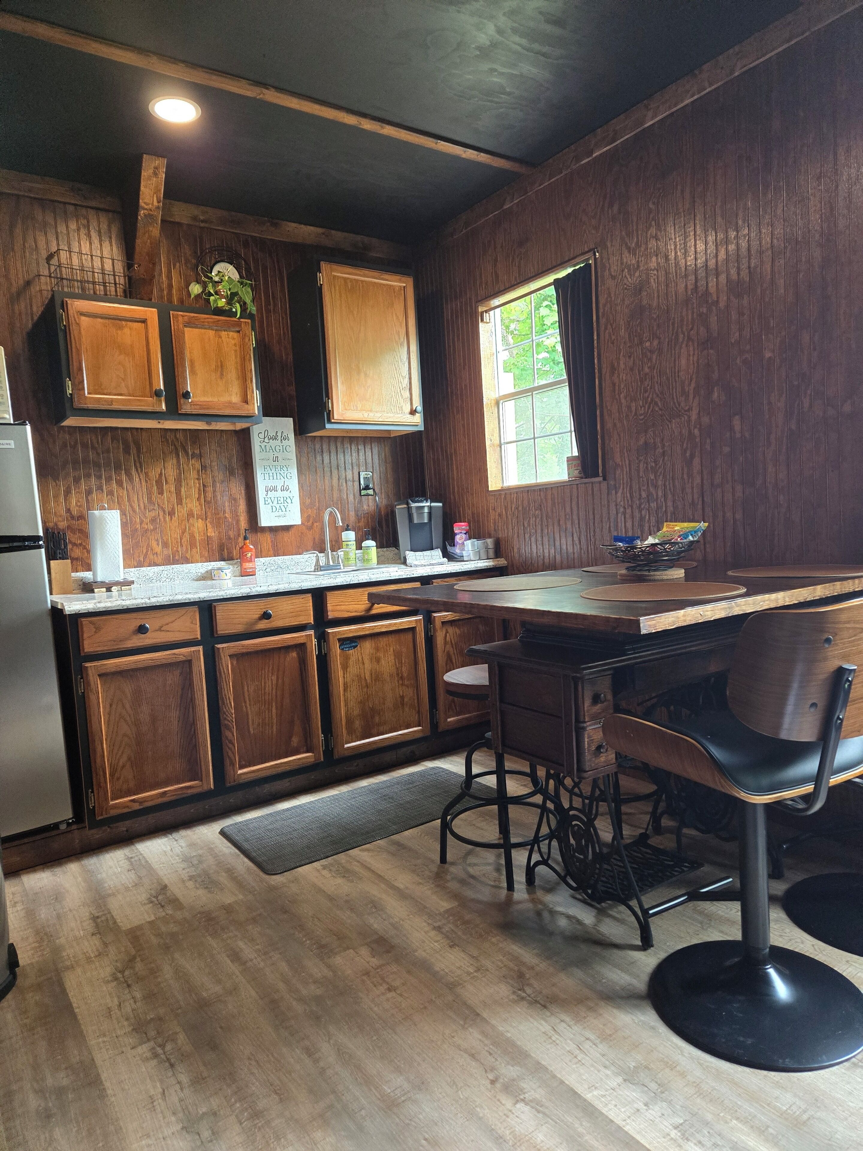 Une cuisine avec des meubles de rangement en bois, un plan de travail, un évier, une machine à café et une fenêtre.