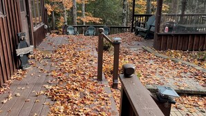 A wooden deck with scattered autumn leaves, a wooden railing, and a bench.