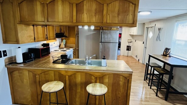 Una cocina moderna con armarios de madera, un refrigerador de acero inoxidable y una zona de bar con taburetes.